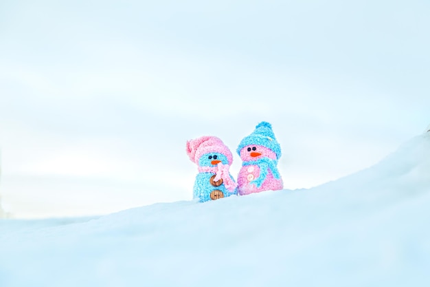 Simpatici pupazzi di neve fatti in casa con sciarpe e cappelli sulla montagna. Racconto d'inverno. Biglietto di auguri con spazio per la copia. Sfondo invernale.
