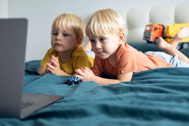 Simpatici ragazzi caucasici ragazzi gemelli che usano il computer portatile a letto a casa bambini che usano la tecnologia