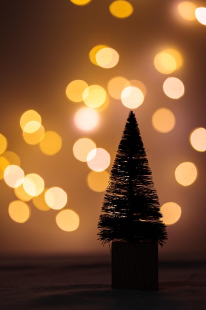 Simpatico albero di abete in miniatura di Natale su un tavolo con luci bokeh al buio