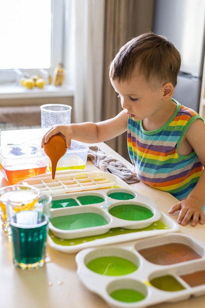 Simpatico bambino che impara a mescolare diversi colori con acqua e vernice in contenitori per lo sviluppo precoce