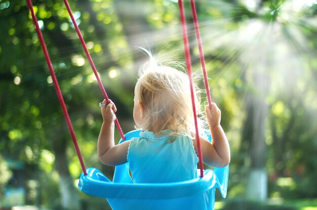 simpatico bambino che oscilla nel parco con alberi ad alto fusto e raggi del sole che arrivano