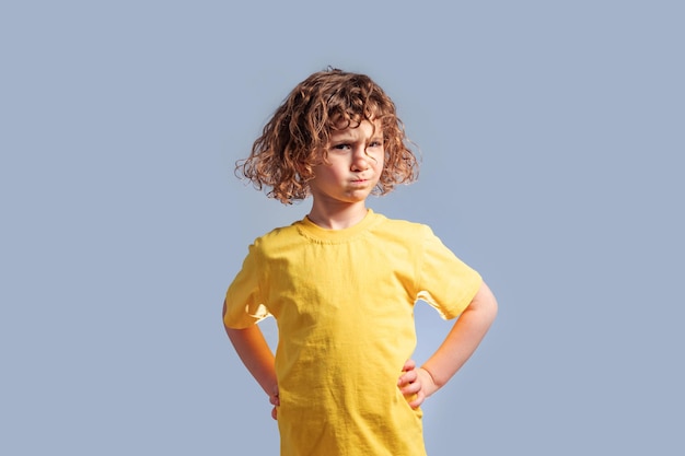 Simpatico bambino di 5 anni con una maglietta gialla che gira la testa sul grigio