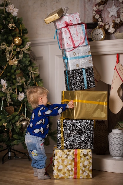 simpatico bambino di tre anni gioca vicino all'albero di Natale con scatole di Natale