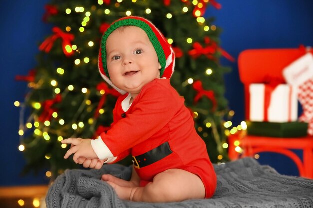 Simpatico bambino in costume da Babbo Natale seduto su sfondo sfocato di luci di Natale