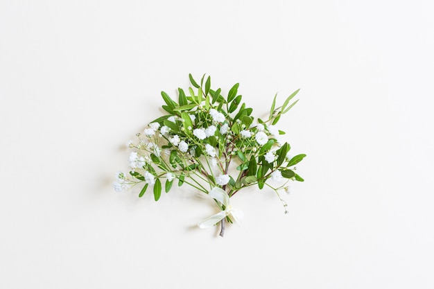 Simpatico bouquet primaverile di ramoscelli con foglie verdi e piccoli fiori di gypsophila. Sfondo pastello chiaro. Concetto di festa della donna, San Valentino, compleanno, vacanze. Affrontare, vista dall'alto, disteso.