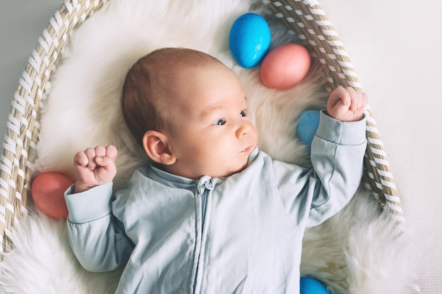 Simpatico coniglietto di Pasqua Piccolo neonato con orecchie da coniglio e uova di Pasqua nel cesto di vimini