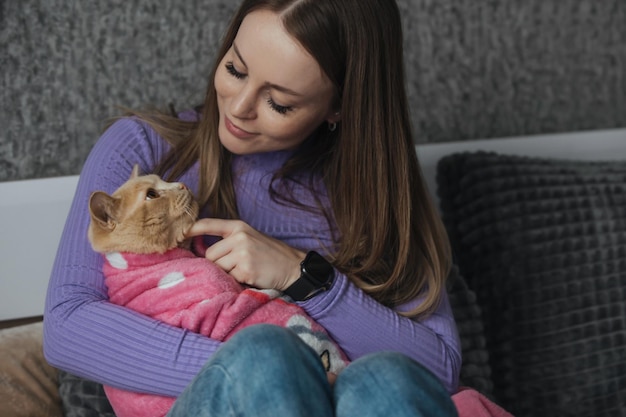 Simpatico gatto domestico avvolto in una coperta per bambini tra le braccia di una giovane donna