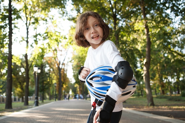 Simpatico ragazzo divertente che fa facce, portando il suo casco dopo aver pattinato nel parco