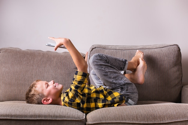 Simpatico ragazzo sorridente che parla con la famiglia e gli amici, fa una videochiamata al telefono, seduto su un divano. Resta a casa, lockdown, distanziamento sociale, quarantena.