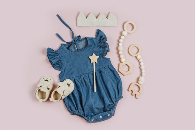 Simpatico set di vestiti per bambini e accessori per ragazza su sfondo rosa. Pagliaccetto blu con coroncina in cotone