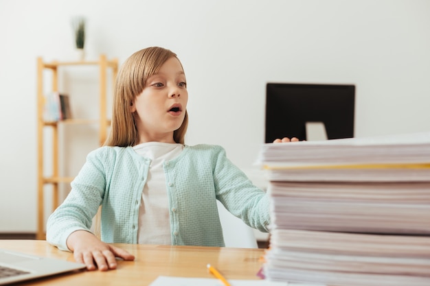 Sincera ragazza emotiva impegnata guardando la pila di carta che ha bisogno di sistemare