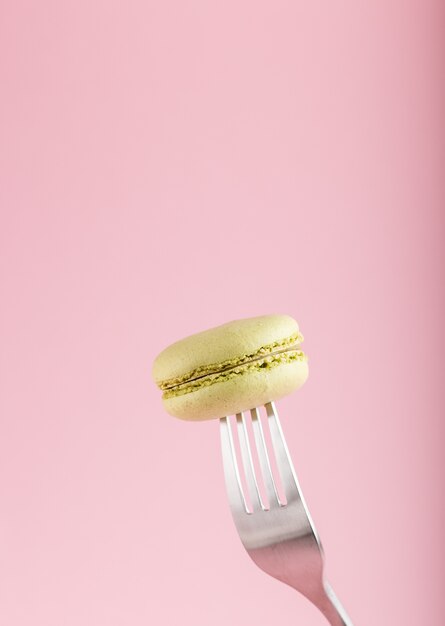 Singolo dolce verde del maccherone o del macaron su una forcella su fondo di rosa pastello. vista laterale.