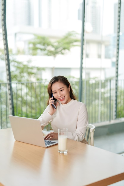 Singolo imprenditore femminile felice con il sorriso sul telefono e lavorando sul computer portatile