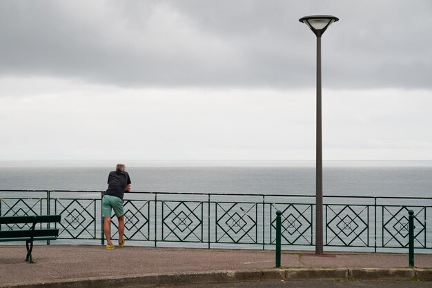 Singolo uomo vista posteriore sulla recinzione anteriore dell'Oceano Atlantico in città Biarritz Paesi Baschi Francia