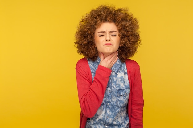 Sintomi influenzali, malattie respiratorie. Ritratto di donna malsana che sussulta per il dolore e tocca il collo doloroso, soffre di mal di gola, infiammazione della laringe. tiro in studio indoor isolato su sfondo giallo