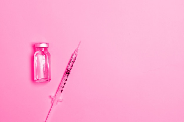 Siringa con medicina dalla fiala di vetro su sfondo rosa vaccinazione