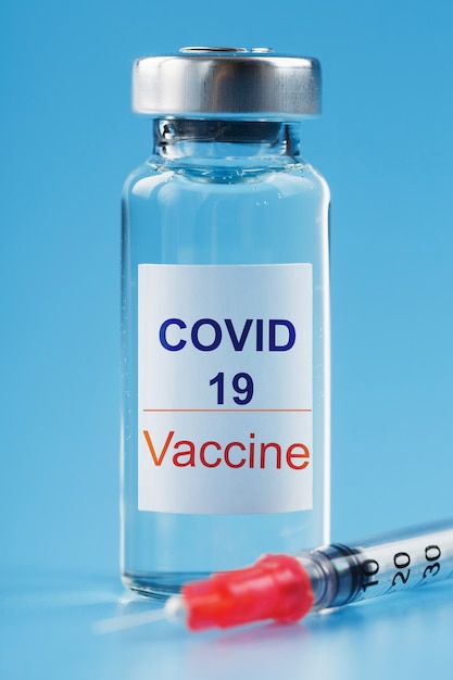 Siringa e fiala con un vaccino contro il virus Covid-19 contro le malattie su sfondo blu.