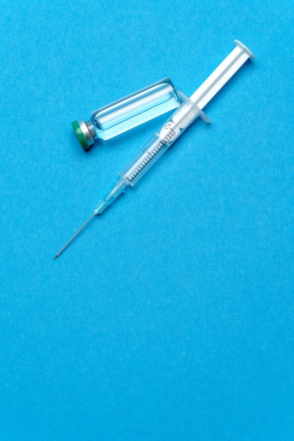 Siringa e fiale con medicinali o vaccini su sfondo blu