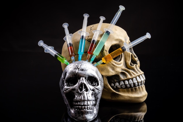 Siringhe colorate si bloccano nel cranio umano su sfondo nero morte dal concetto di uso di droghe