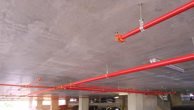 Sistema di tubazioni dell'acqua di protezione antincendio rosso sul soffitto in cemento all'interno dell'edificio del garage