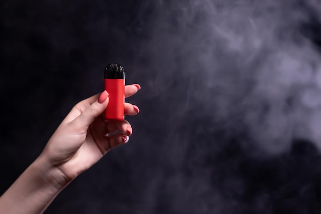 Sistema di vape pod di colore rosso con cartucce sostituibili in mani femminili isolate su sfondo nero Il concetto di fumo moderno vaping e nicotina Sullo sfondo del fumo