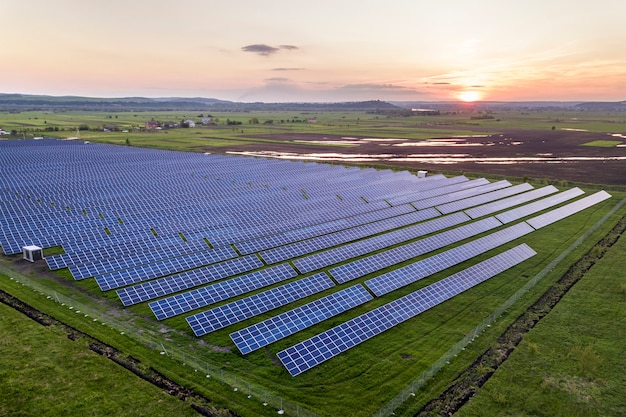 Sistema solare blu dei pannelli fotovoltaici della foto che produce energia pulita rinnovabile su paesaggio rurale e sul fondo del tramonto.