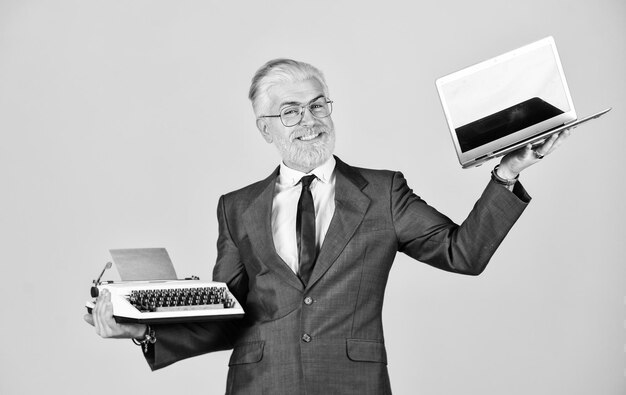 Sito educativo computer o macchina da scrivere nuova e vecchia tecnologia moderna digitale business vintage macchina da scrivere felice uomo d'affari uso retrò macchina da scrivere e moderno laptop uomo maturo capelli tinti barba