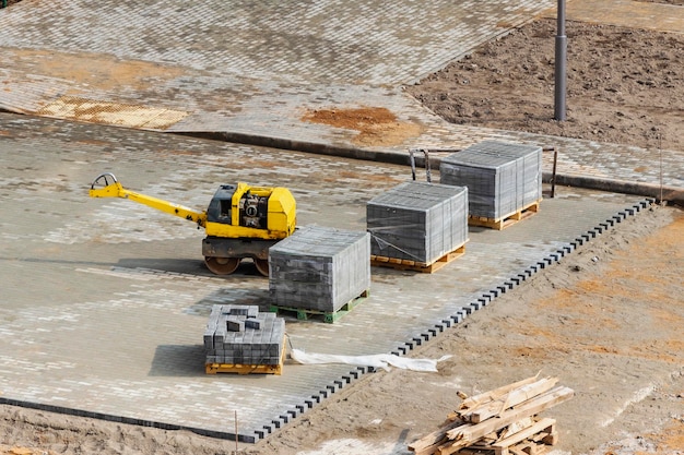 Sito predisposto per la posa di lastre di pavimentazione Rullo a mano per la compattazione Lastre di pavimentazione grigie su pallet Vista dall'alto