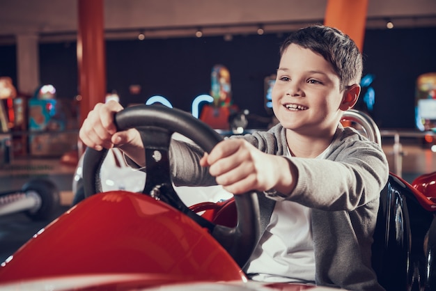 Sittng felice del bambino in automobile del giocattolo nel centro di divertimento