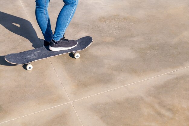 Skateboard e piedi di una persona irriconoscibile su un pavimento di cemento