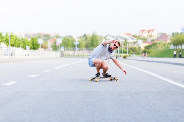 Skateboarder in occhiali da sole cavalca longboard su strada asfaltata in città