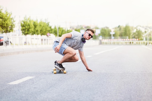 Skateboarder in occhiali da sole cavalca longboard su strada asfaltata in città