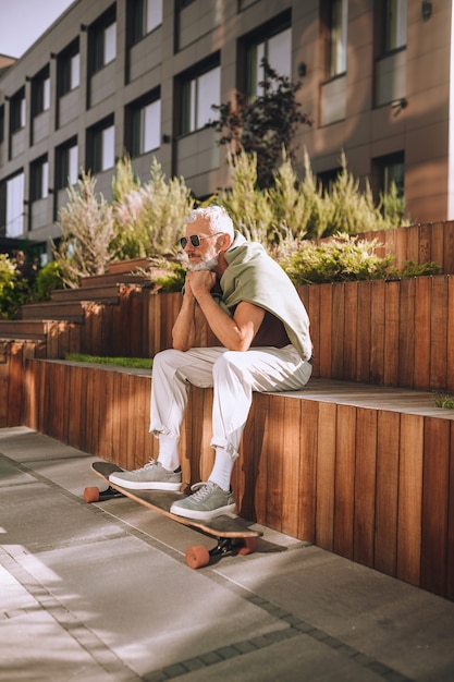 Skateboarder maschio con i piedi sullo skateboard seduto fuori