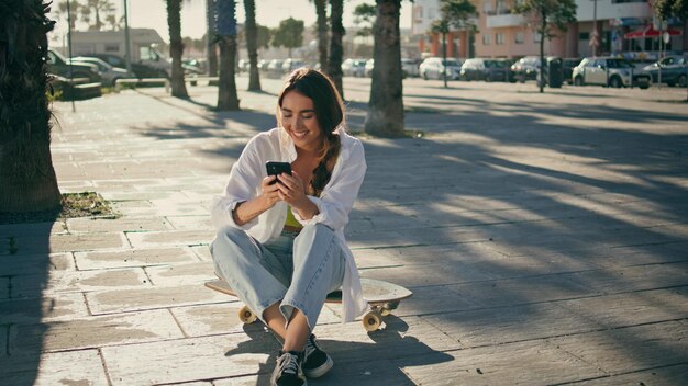 Skater spensierato che fa un selfie con il telefono al sun alley donna sportiva seduta su un longboard