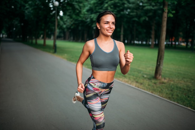 Slim donna fare jogging sul marciapiede nel parco estivo. Corridore femminile sull'allenamento mattutino all'aperto