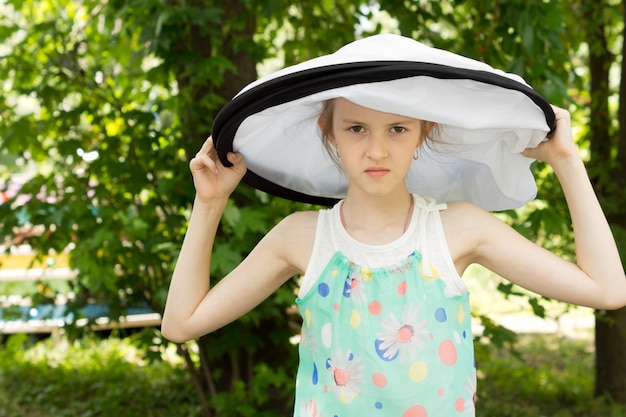 Slim giovane ragazza abbastanza pazza in grande cappello bianco rotondo su sfondo naturale Nature