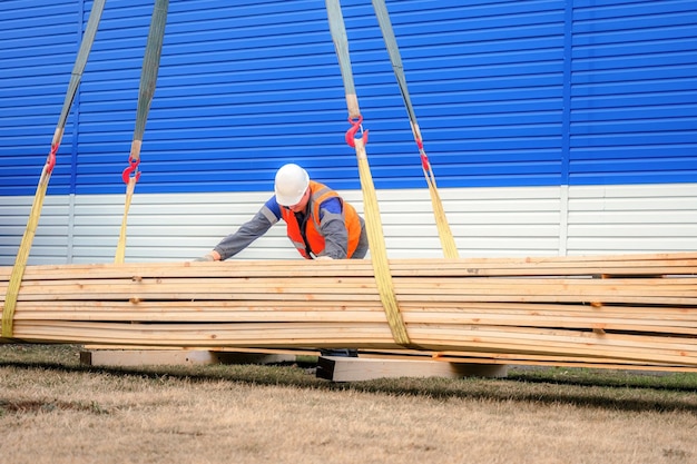 Slinger in casco e giubbotto di segnalazione scarica assi di legno all'esterno il giorno d'estate