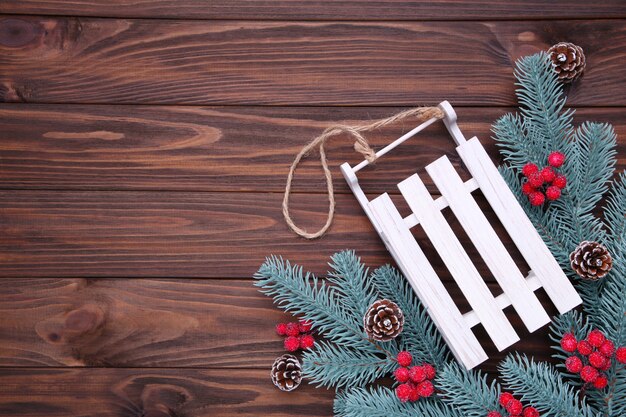 Slitta giocattolo di Natale con ramo di abete su uno sfondo marrone.