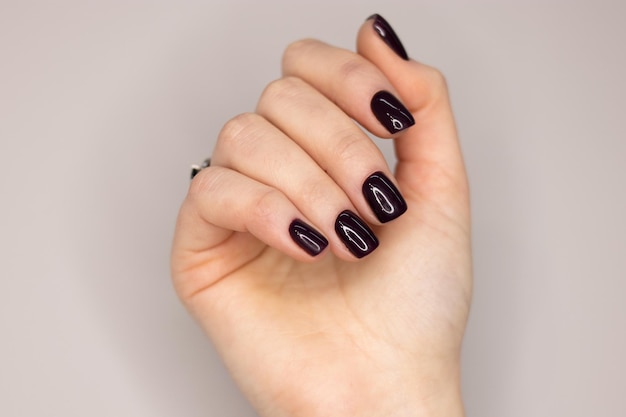 Smalto gel scuro sulle unghie di una ragazza. Manicure scura con unghie quadrate morbide. Rivestimenti in smalto gel.