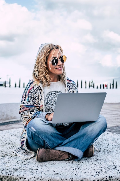 Smart working e digital nomad people concetto di stile di vita con allegra felice e libera donna caucasica che lavora all'aperto con il computer portatile sulle gambe persone moderne e connessione tecnologica