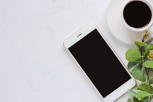 Smartphone con il mazzo della foglia e della tazza di caffè su fondo di marmo bianco