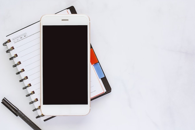 Smartphone con il taccuino a spirale e penna nera su fondo di marmo