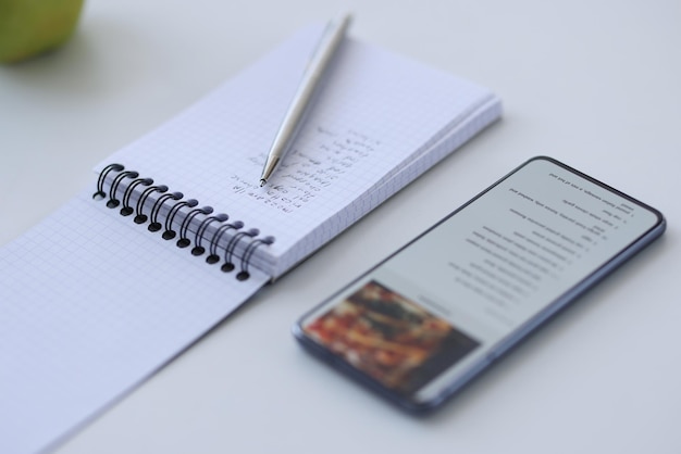 Smartphone con ricetta e taccuino con appunti didattici di cucina e app mobile con ricette