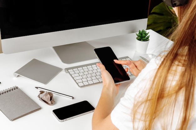 Smartphone con schermo nero in mani femminili. Computer, tastiera e forniture per ufficio