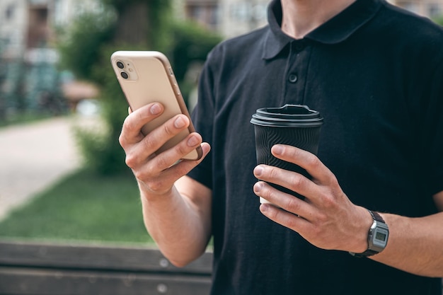 Smartphone del primo piano e un bicchiere di caffè nelle mani di un uomo