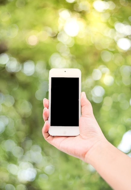 smartphone della holding della mano della donna con la priorità bassa verde del bokeh