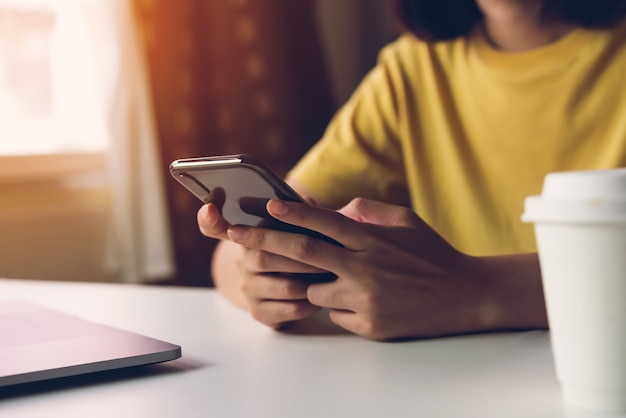 Smartphone della tenuta della donna, facendo uso del telefono cellulare sul caffè.