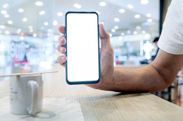 Smartphone della tenuta della mano dell'uomo del primo piano con lo schermo bianco in bianco mentre sedendosi al caffè, schermo in bianco per progettazione del graphinc.