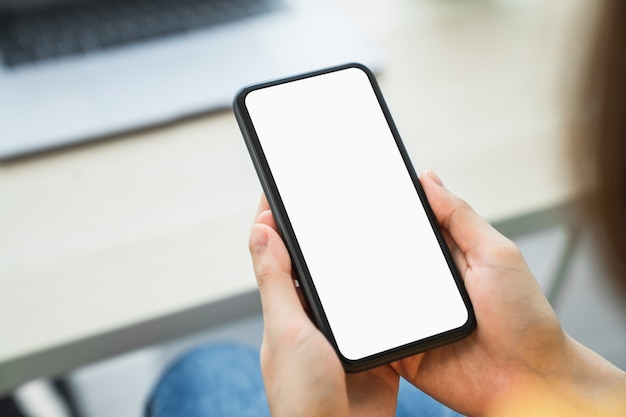 Smartphone della tenuta della mano della donna e schermo in bianco commovente. Mockup di pubblicità.