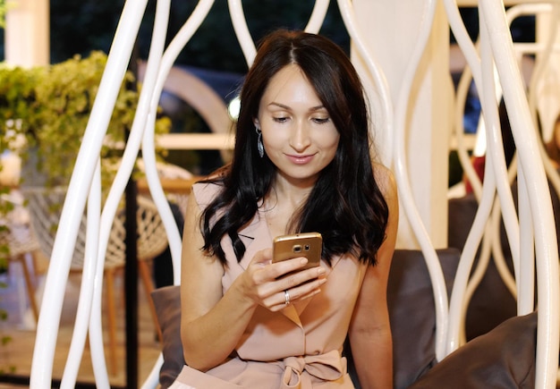 Smartphone di navigazione di giovane bella ragazza che si siede al bar. Sta toccando lo schermo e sorride. Modi moderni di concetto di comunicazione.